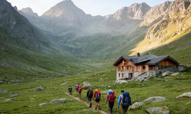 Senderistas cruzando un valle de los Pirineos junto a un refugio de montaña